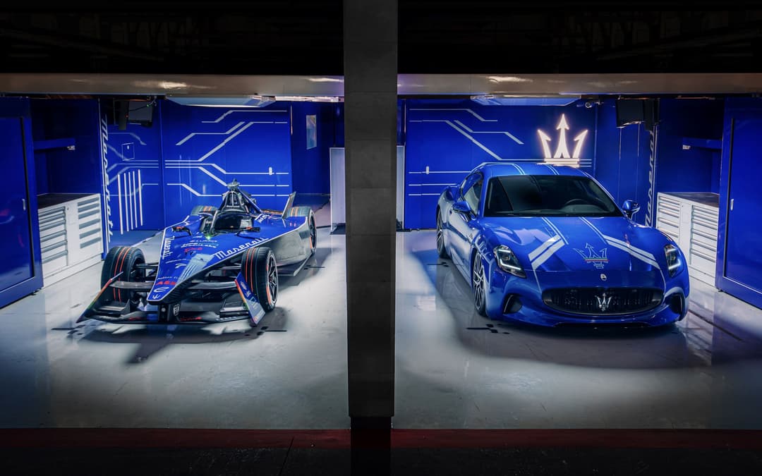 Monoplaces de Formule E Maserati et voiture de route Maserati bleues alignées dans un garage illuminé aux néons bleus