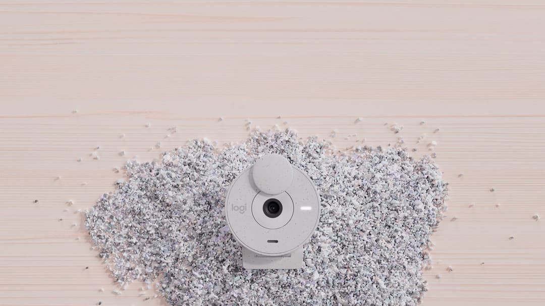 Webcam Logitech Brio 305 blanche vue de face, entourée de confettis argentés sur fond bois clair