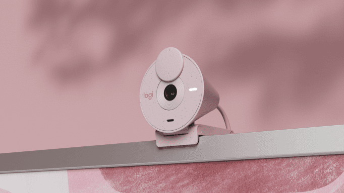 Webcam Logitech Brio 300 blanche au design conique, fixée sur un écran, fond rose