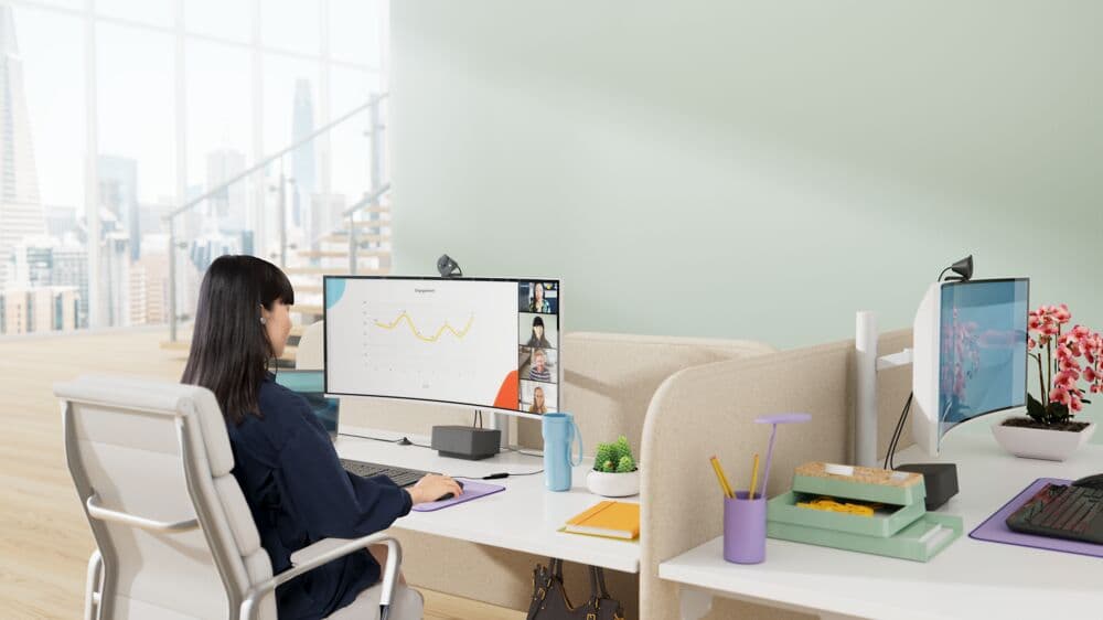 Femme en visioconférence sur son bureau avec webcam Logitech Brio 305 montée sur moniteur, vue de skyline en arrière-plan