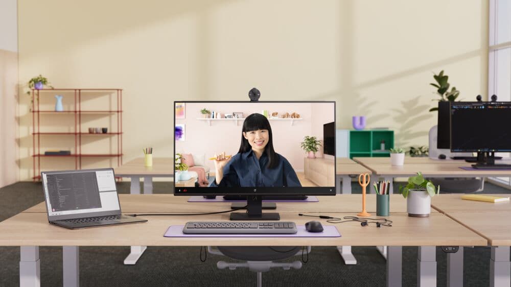 Webcam Logitech Brio 300 montée sur un écran de bureau, capturant une femme souriante en visioconférence dans un bureau lumineux