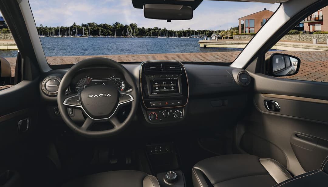 Habitacle de la Dacia Spring Extreme avec détails brun cuivré sur le volant, les aérateurs et les panneaux de porte, vue depuis le siège conducteur