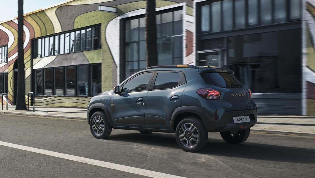 Dacia Spring gris foncé finition Extreme en stationnement devant un bâtiment moderne aux façades colorées