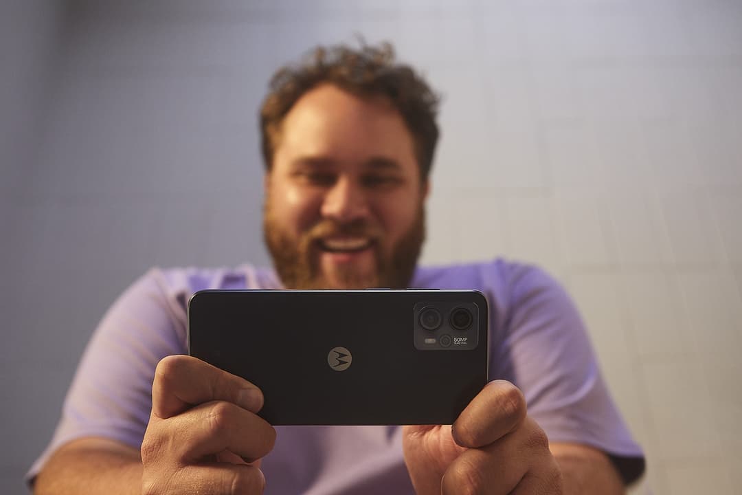 Homme tenant un smartphone Motorola noir avec double caméra arrière, souriant devant l'appareil