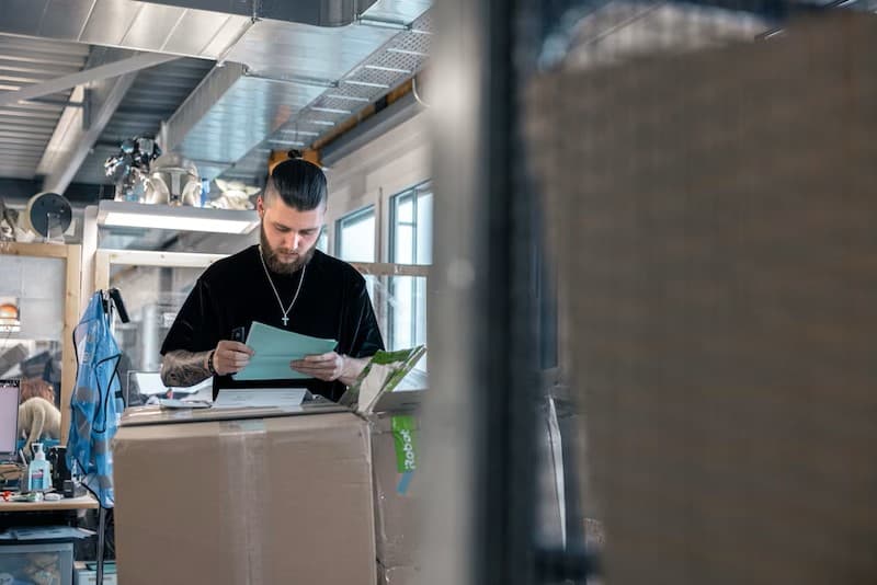 Employé du service après-vente de Digitec Galaxus examinant une tablette tactile au-dessus d'un colis cartonné dans un atelier