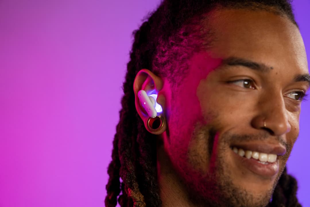 Logitech G FITS, écouteur gaming true wireless blanc et rose fluo porté à l'oreille, fond dégradé rose et violet