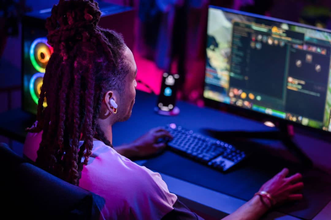 Gamer portant les écouteurs Logitech G FITS assis devant un écran, avec clavier illuminé et ambiance RGB bleue et rose