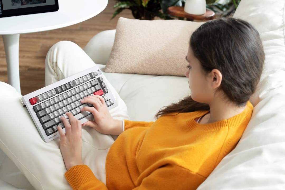 Personne en pull orange utilisant un clavier Keychron blanc et gris assis sur un canapé