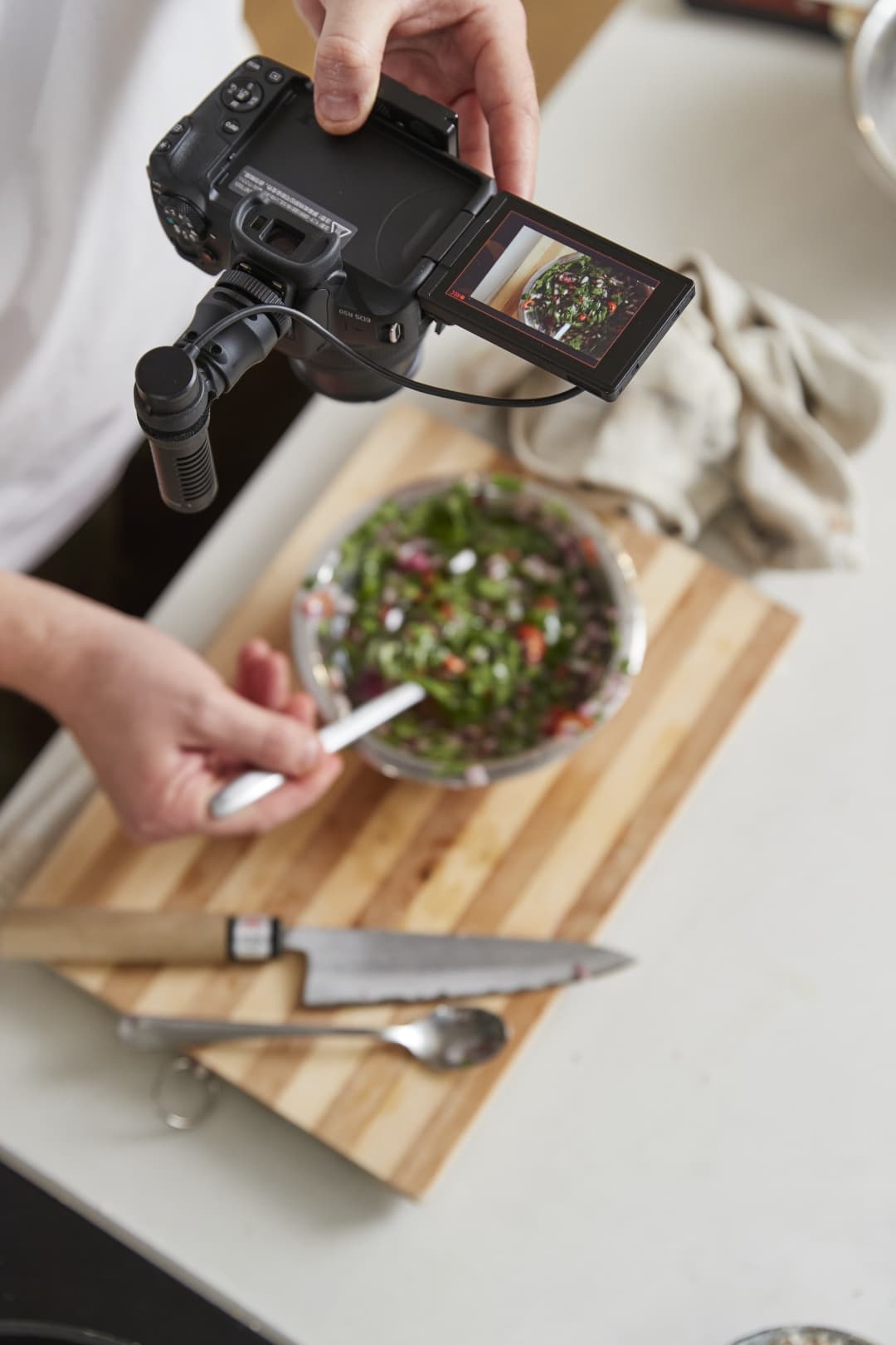 Canon EOS R50 avec microphone externe raccordé, filmant une salade sur une planche à découper en bois