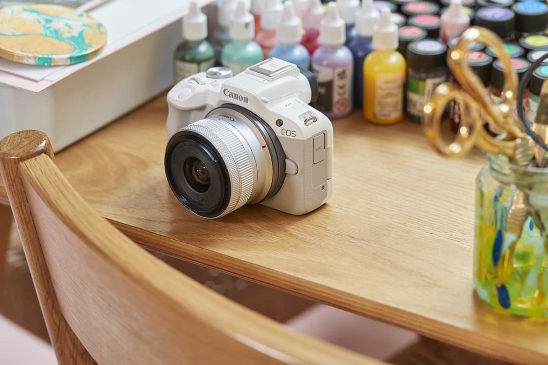 Canon EOS R50 blanc avec objectif RF-S 18-45mm posé sur un bureau en bois entouré de fournitures créatives