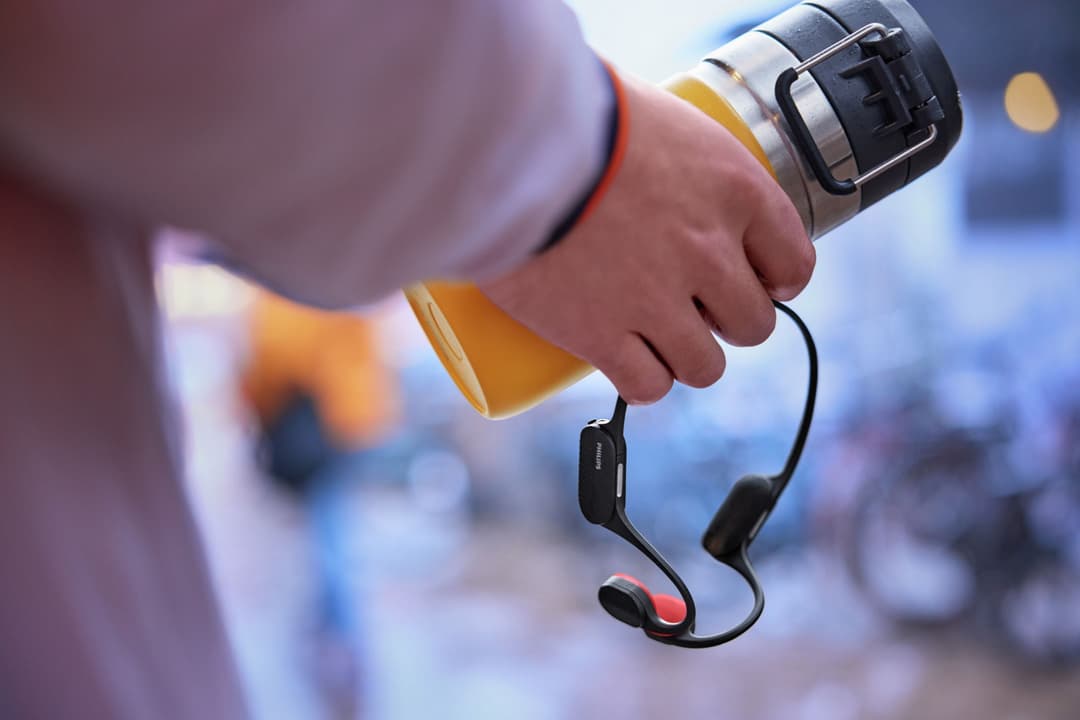 Casque Philips GO Sport TAA5608 noir avec détails rouges, tenu à la main avec un tour de cou gris et jaune