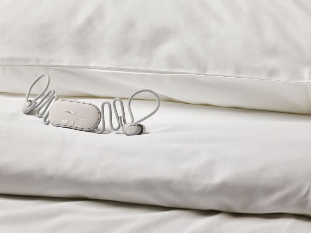 Écouteurs Philips Sleep Buds N7808 blancs posés sur des draps et un oreiller