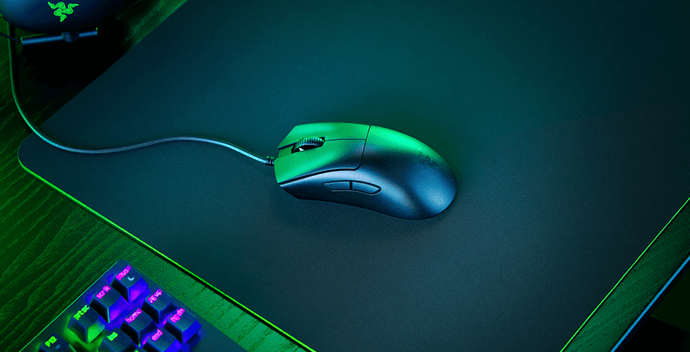 Souris Razer DeathAdder V3 Pro aux couleurs vert et bleu avec câble tressé, posée sur un tapis gamer à côté d'un clavier mécanique