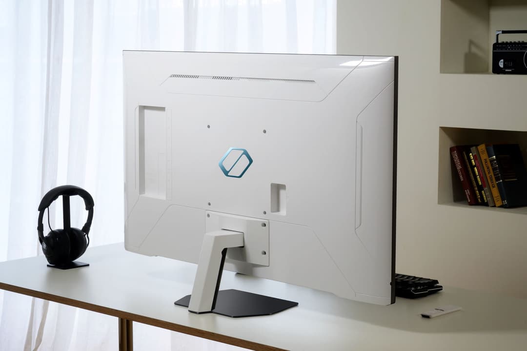 Écran de jeu Samsung Odyssey Neo G70C blanc de face, posé sur un bureau avec un casque audio noir à côté