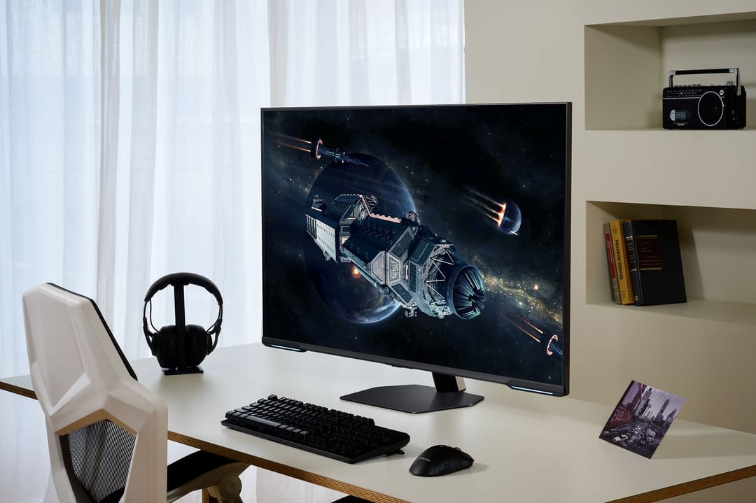 Samsung Odyssey Neo G70C affichant une scène de science-fiction spatiale sur un bureau avec casque, clavier et souris noirs