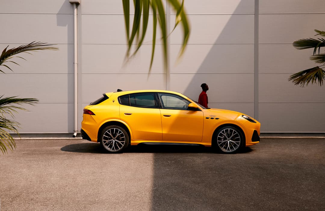 Maserati de couleur or garée devant une façade beige, avec une personne en veste rouge à proximité