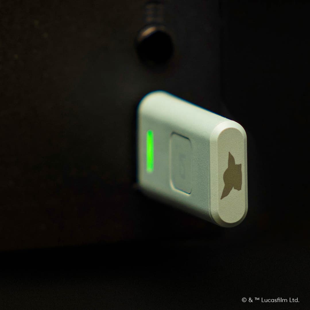 Détail du casque audio Logitech G A30 The Mandalorian™ Edition montrant l'étiquette de haut-parleur personnalisée avec le profil du Mandalorien et le sigle du Clan Mudhorn, voyant vert allumé