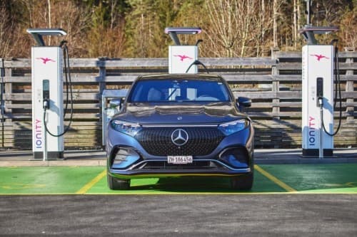 Mercedes bleu électrique en charge sur une borne publique, stationnée devant une barrière en bois