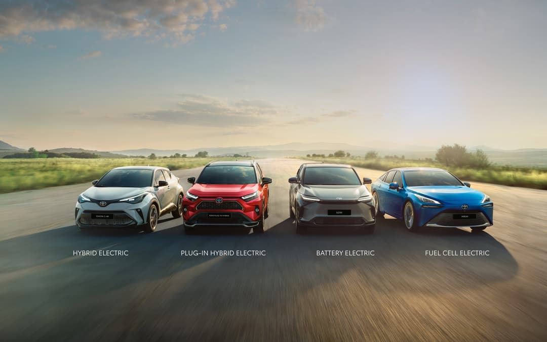 Quatre véhicules Toyota alignés sur une route, de gauche à droite : hybride électrique gris, hybride rechargeable rouge, électrique batterie gris, pile à combustible bleu