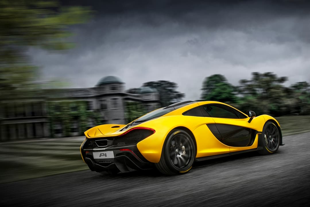 McLaren P1 jaune en mouvement sur route, vue de profil trois-quarts, mettant en évidence sa silhouette aérodynamique et ses formes épurées