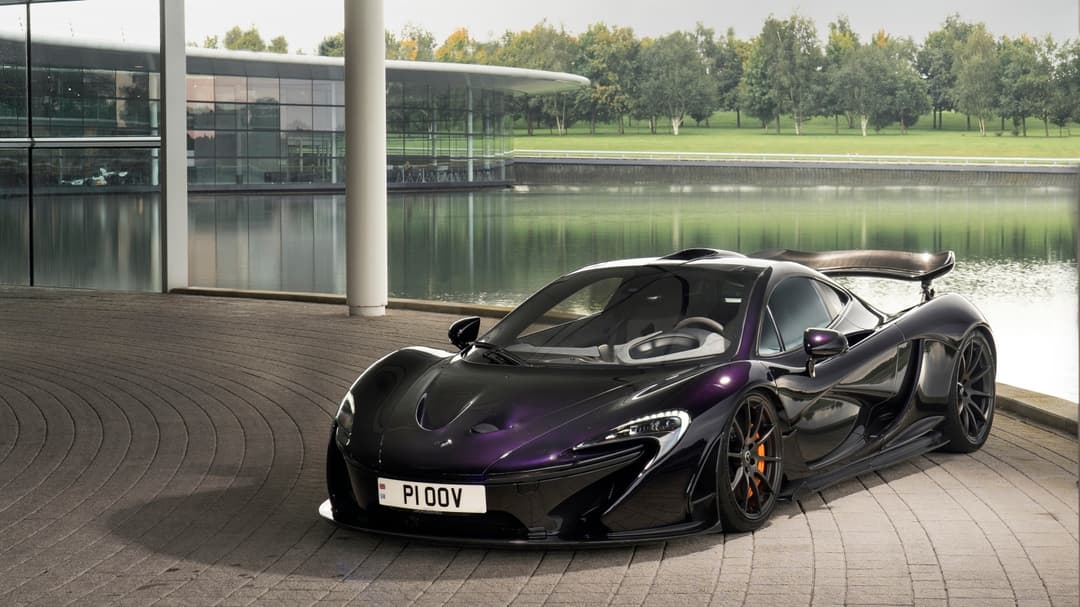 McLaren P1 noire avec aileron arrière profilé, garée sur une terrasse près d'un lac