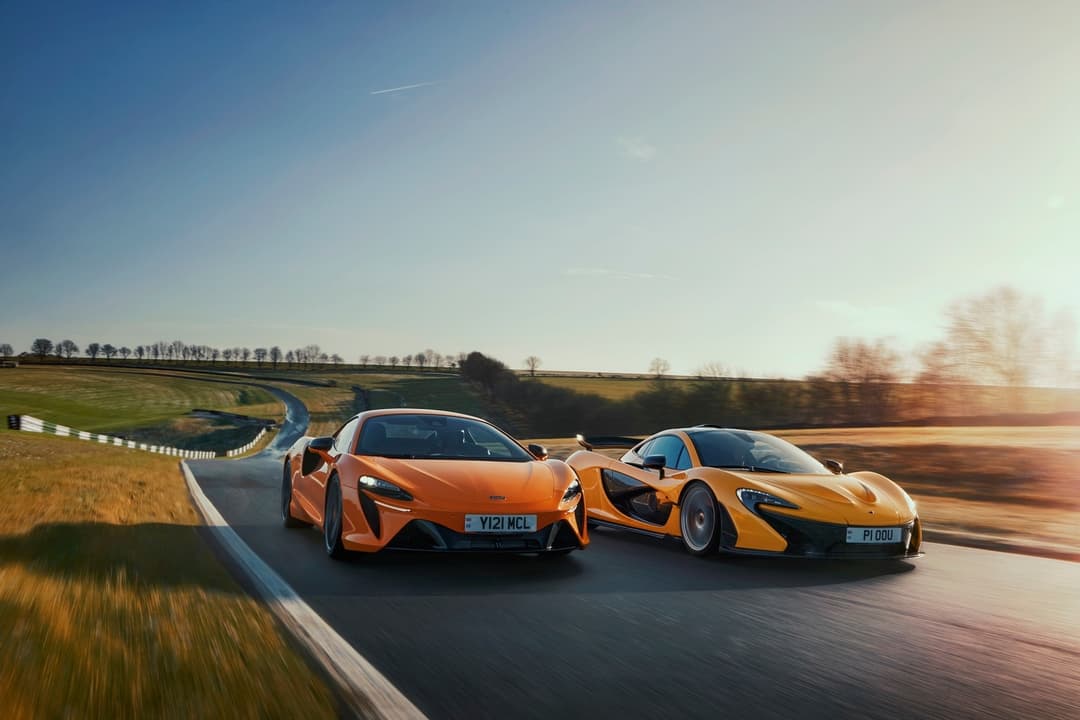 McLaren Artura orange et McLaren P1 jaune/or en mouvement sur route campagnarde