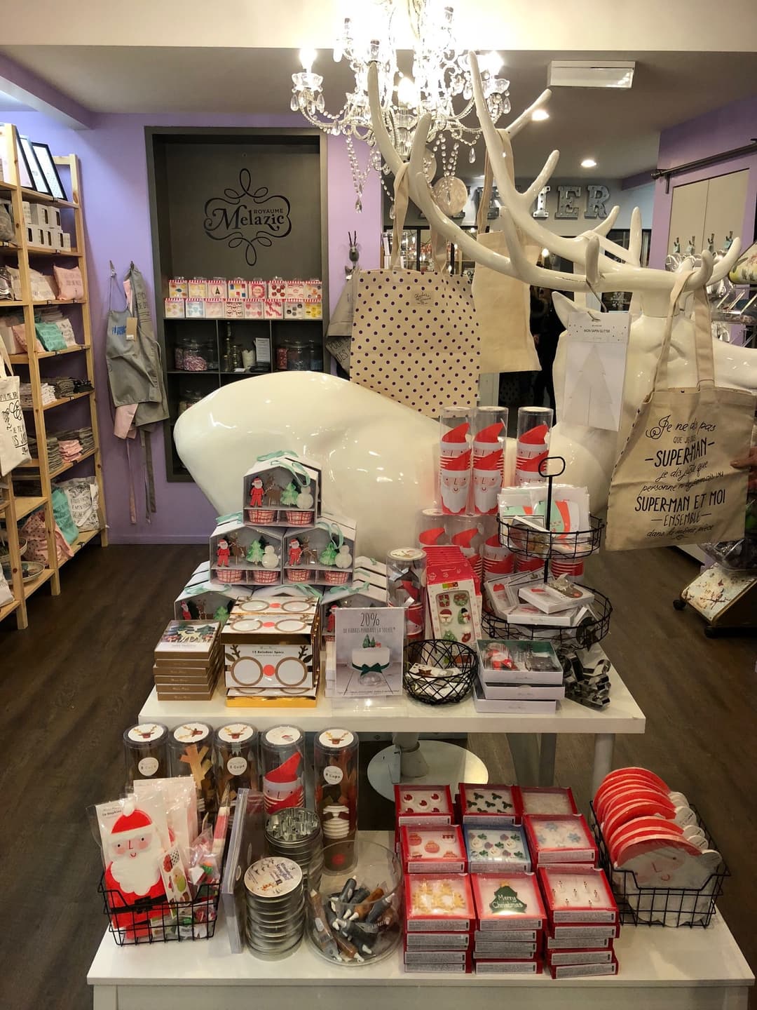 Boutique Melazic décorée pour Noël avec vitrines de cupcakes, branche blanche ornementale, articles rouges et verts, mobilier de rangement et lustre en cristal