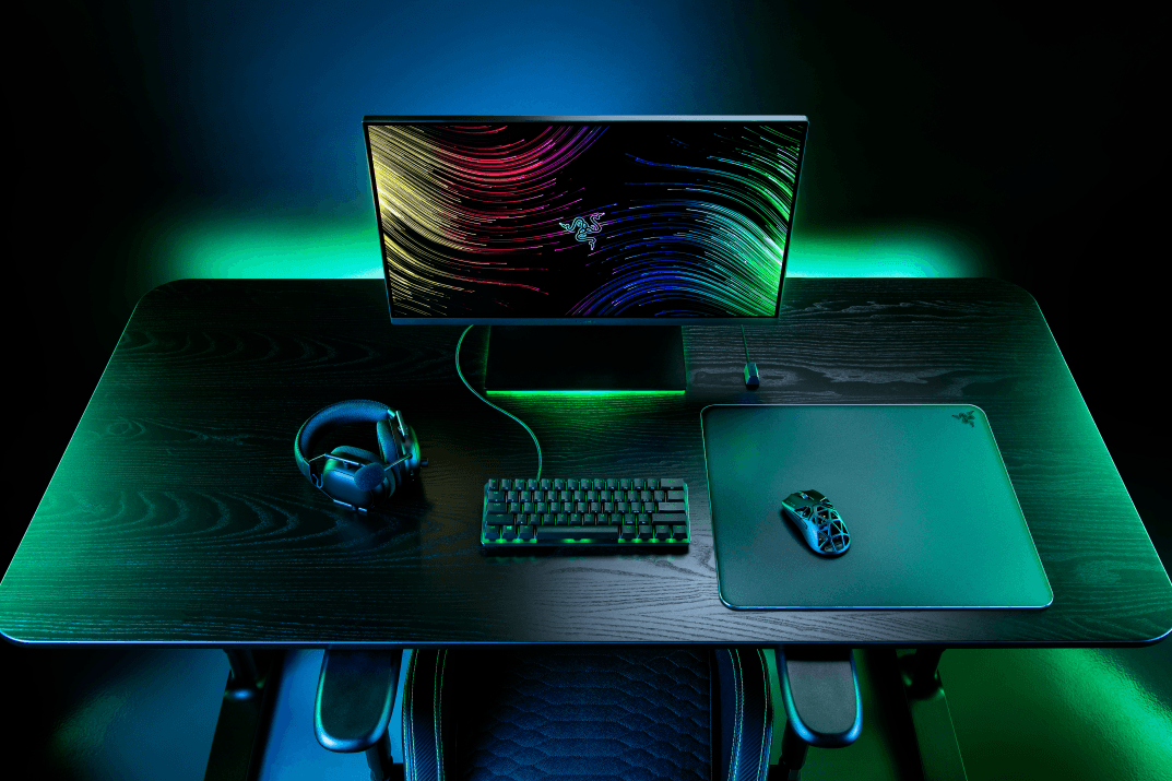 Tapis de souris Razer Atlas en verre trempé sur un bureau gaming illuminé en vert et bleu, entouré d'un casque, clavier et souris Razer