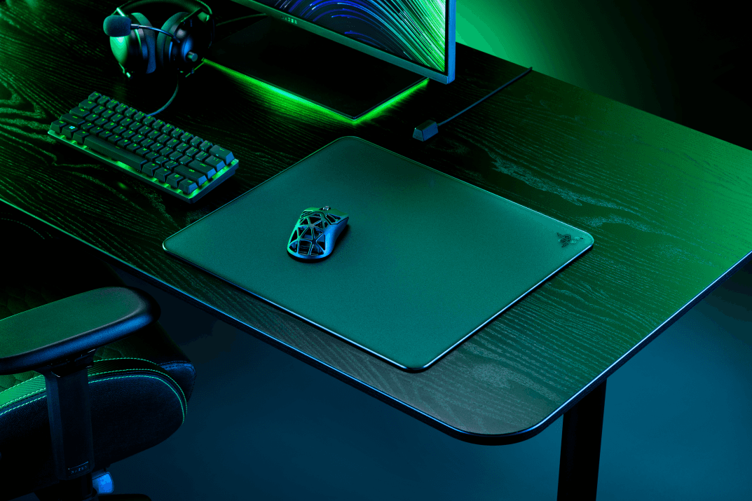 Tapis de souris Razer Atlas en verre trempé avec souris gaming posée dessus, dans un setup gaming illuminé en vert et bleu