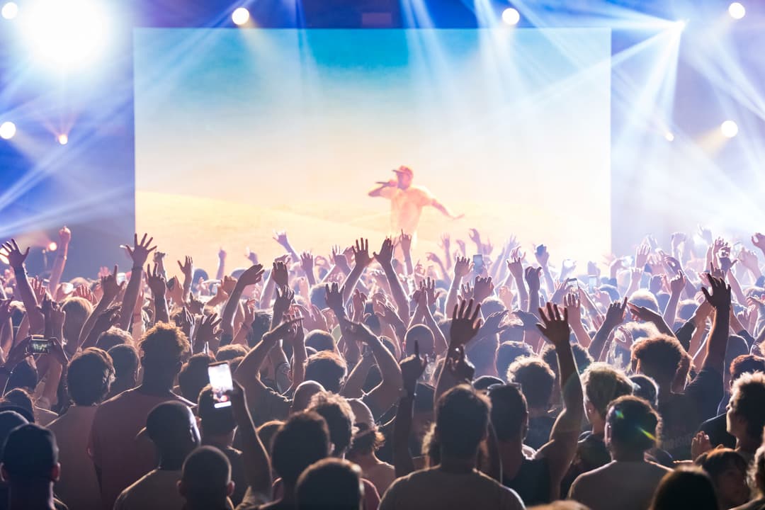 Artiste sur scène devant une foule en délire au Montreux Jazz Festival, mains levées et téléphones brandis, éclairage bleu et or
