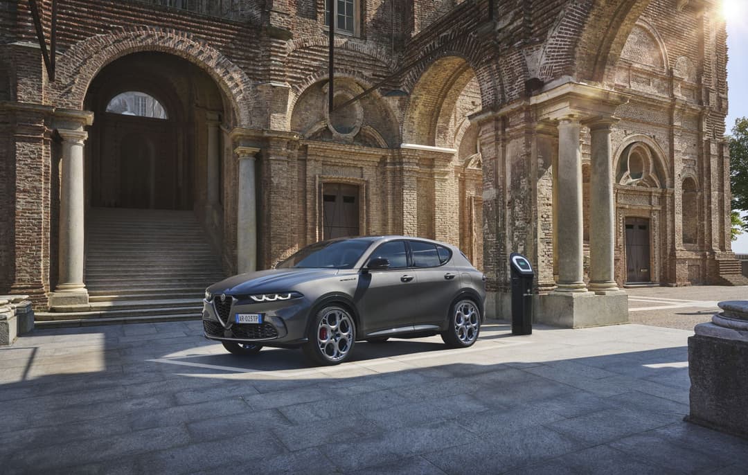 Alfa Romeo Tonale Hybride Rechargeable Q4 gris, stationnée devant une église en brique avec arcades, borne de recharge visible