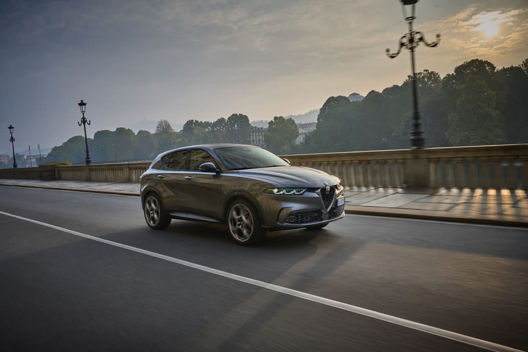 Alfa Romeo Tonale Hybride Rechargeable gris métallisé en mouvement sur un pont urbain entouré de végétation
