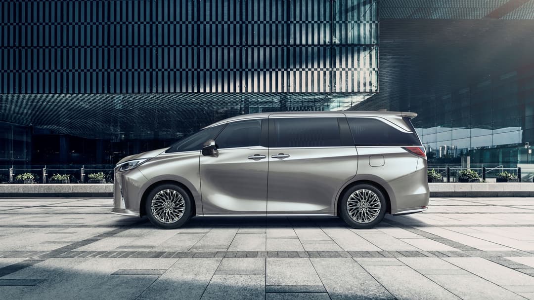 Lexus LM argent gris, monospace luxe spacieux, garé de profil sur une place devant architecture moderne