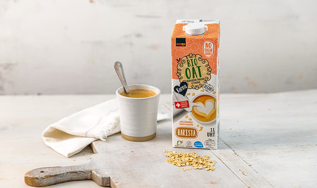 Brique de boisson à l'avoine bio Coop à côté d'une tasse de café et de flocons d'avoine éparpillés