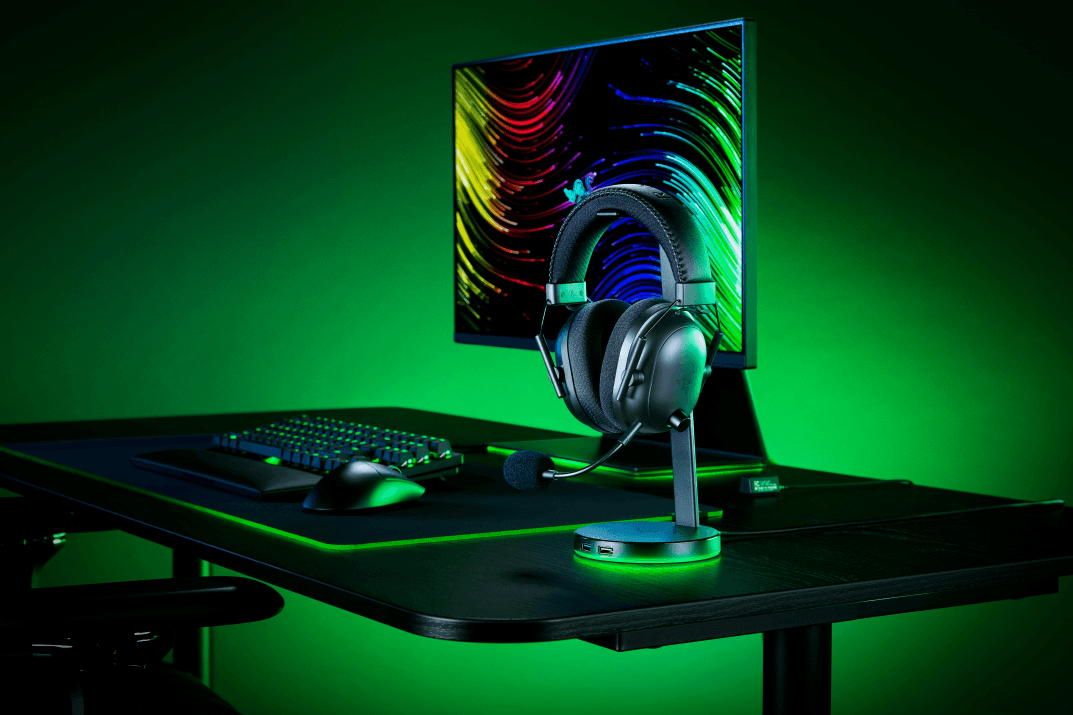 Casque Razer Blackshark V2 Pro 2023 sur son socle, posé près d'un clavier et d'une souris gaming, devant un écran, ambiance verte