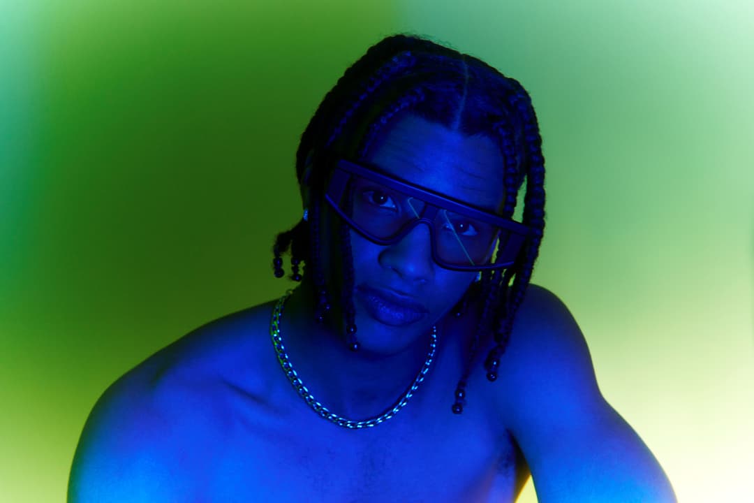 Personne portant des lunettes de soleil noires avec verres teintés, sur fond dégradé bleu et vert