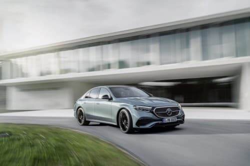 Mercedes-Benz Classe E bleu clair en mouvement devant un bâtiment moderne aux façades vitrées