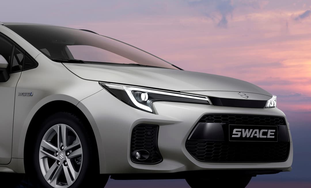 Suzuki Swace blanche berline compacte en trois quarts avant sur fond de ciel rose et mauve au coucher du soleil
