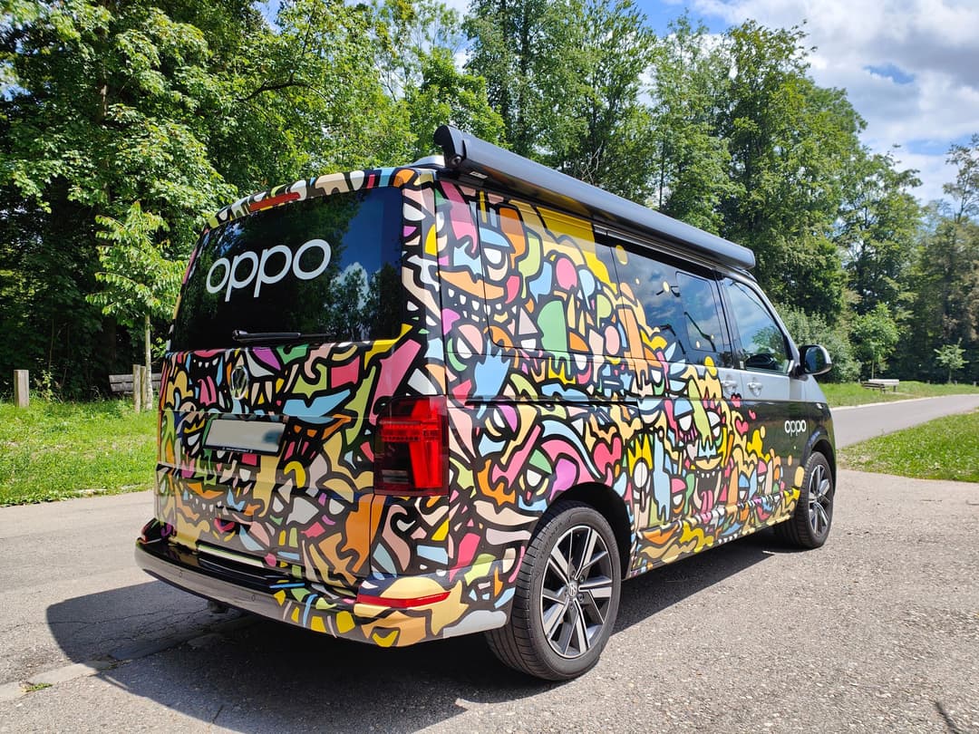 Bus OPPO aux couleurs vives et motifs graphiques multicolores circulant sur une route entourée de végétation