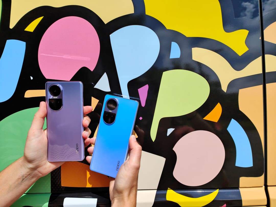 Deux smartphones Oppo Reno10, un violet et un bleu, tenus en main devant une fresque murale colorée