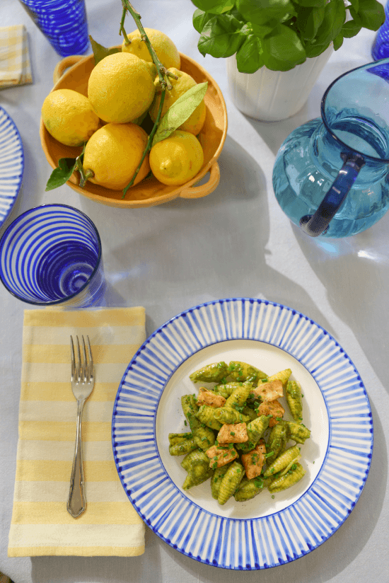 Pâtes nappées de pesto Basilico e Limone dans une assiette à bord bleu, entourée de citrons frais et de basilic vert