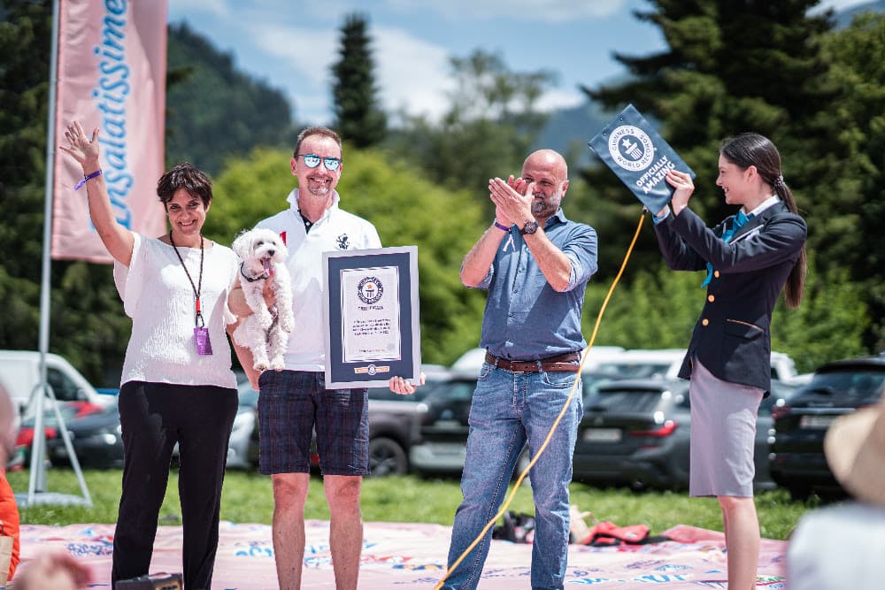 Quatre personnes célèbrent avec un certificat Guinness World Record lors d'un pique-nique en montagne, l'une d'elles tenant un petit chien blanc