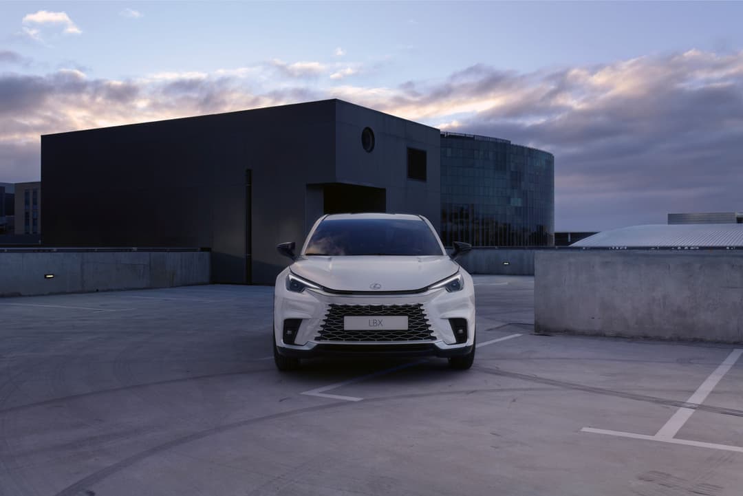 Lexus LBX blanc de face sur un toit-terrasse béton, bâtiments modernes en arrière-plan au crépuscule