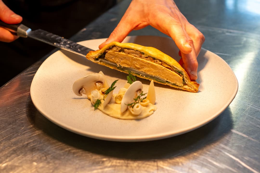 Filet de poulet végétal Planted doré sur assiette blanche, tranché au couteau par une main, accompagné de champignons et herbes