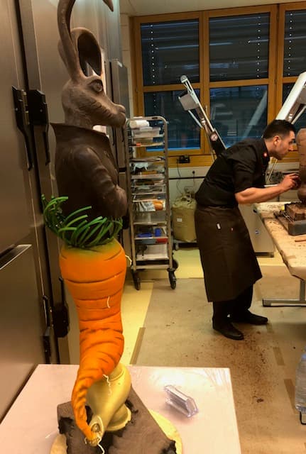 Jorge sculpteur chocolatier travaillant dans son atelier, avec une grande sculpture de lapin en chocolat aux mains de bronze à proximité