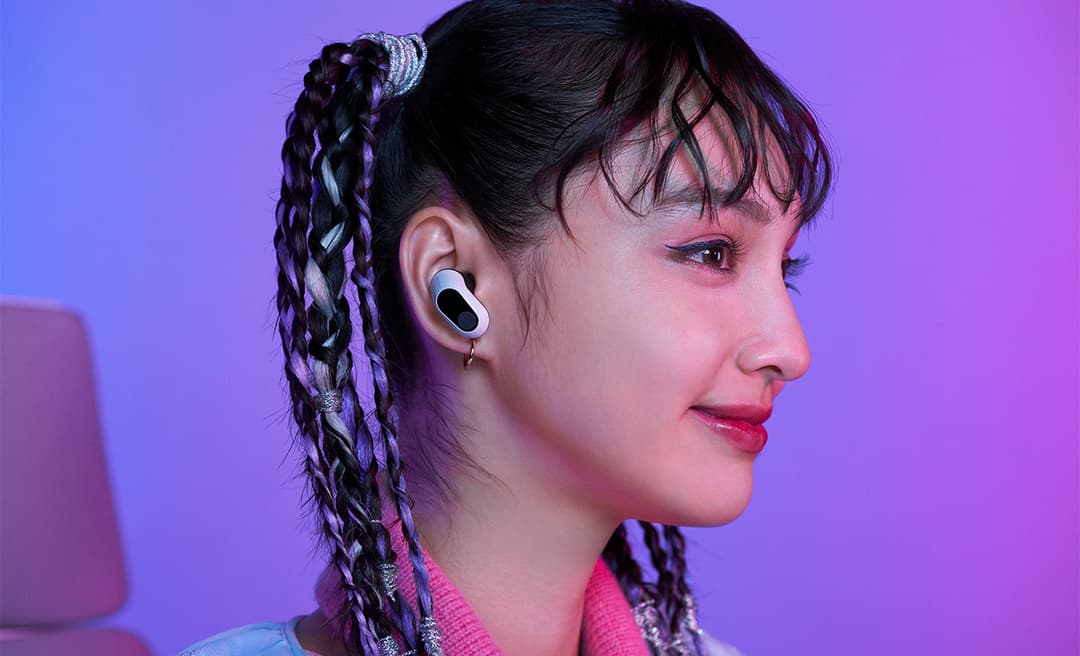 Écouteur sans fil Sony INZONE Buds blanc dans l'oreille d'une femme en profil, fond rose et bleu dégradé