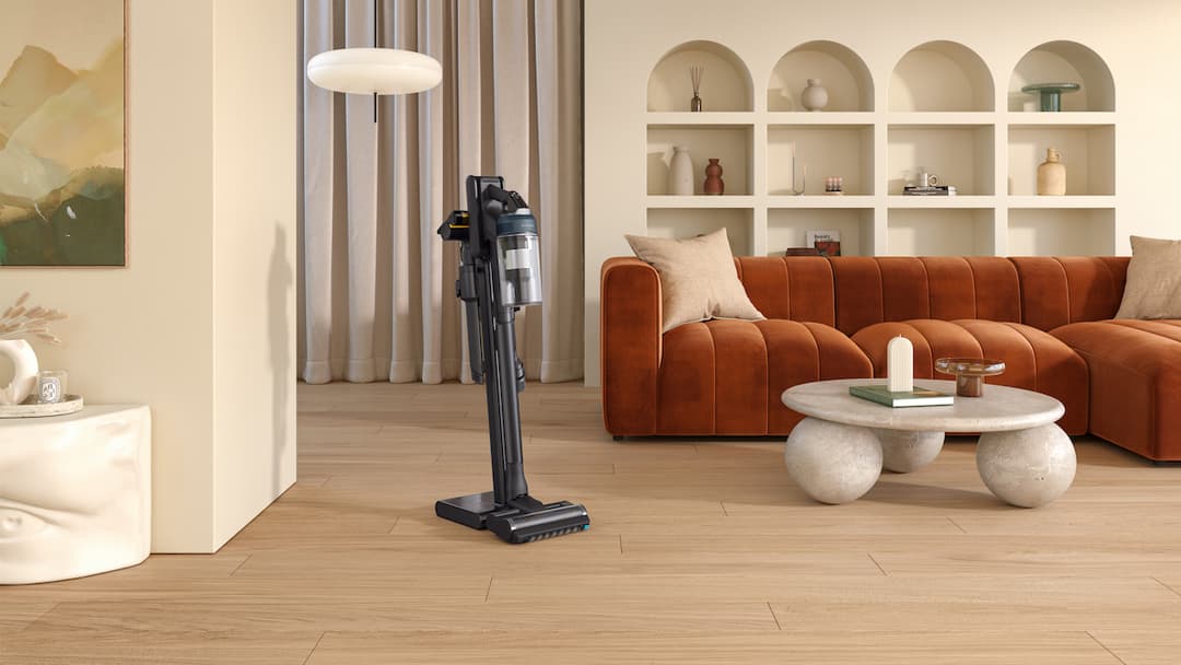 Aspirateur Samsung Jet sans fil posé sur son support dans un salon moderne avec canapé terracotta et sol en bois
