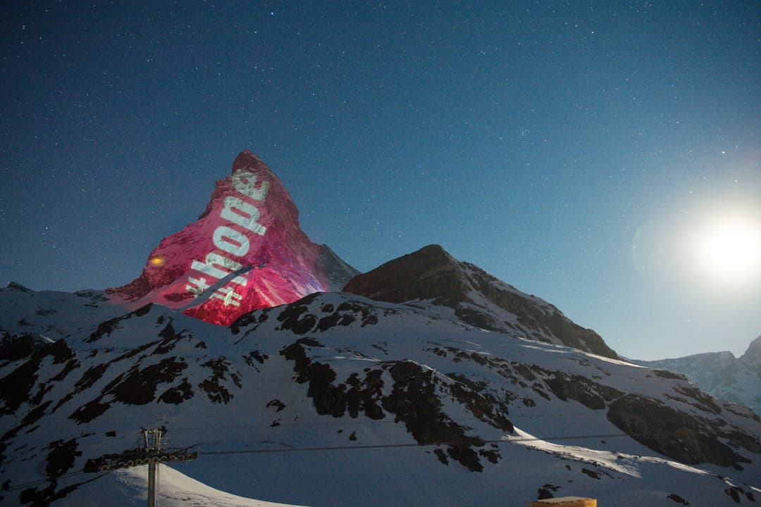 Projection d'un Père Noël géant en rouge et blanc sur la montagne enneigée des Rochers-de-Naye, ciel étoilé bleu-teal