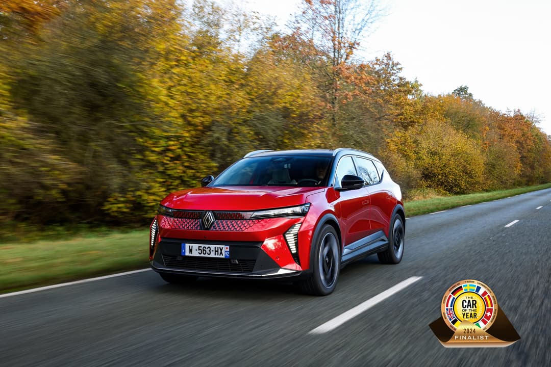 Renault Scenic E-Tech électrique rouge en mouvement sur route, avec forêt d'automne en arrière-plan et logo Car of the Year 2024 Finalist en bas à droite