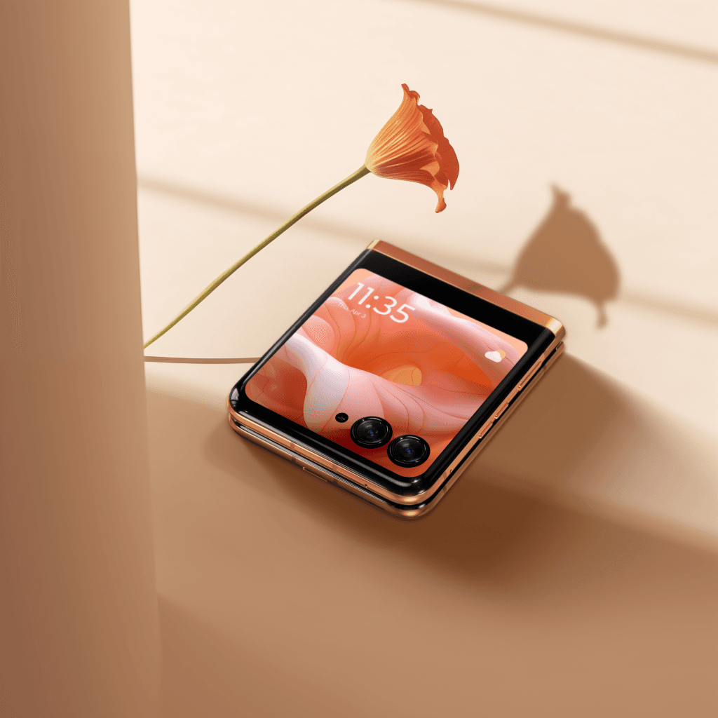 Motorola razr40 Ultra couleur pêche, téléphone à clapet ouvert, à côté d'une fleur orange sur fond beige